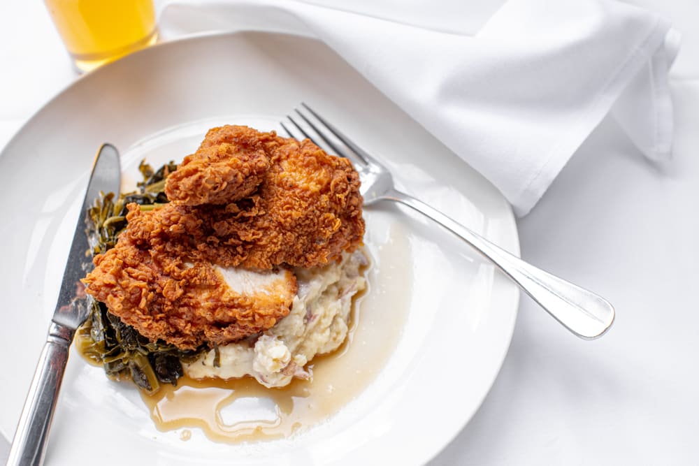 A plate of fried chicken with greens and mashed potatoes, served with a fork and knife in Atlanta, Georgia.
