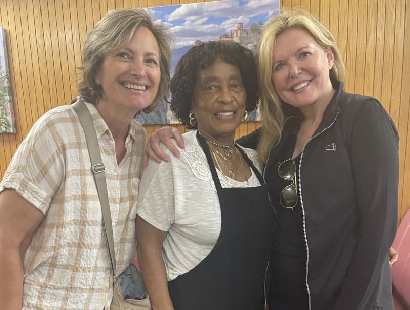 Three smiling women stand together, arms around each other, in a room with wooden paneling in Atlanta, Georgia.