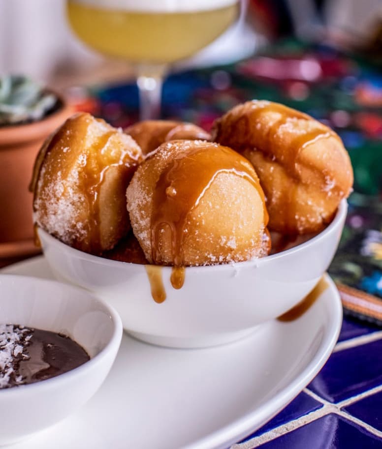 Golden-brown doughnut holes with caramel drizzle and powdered sugar, served with chocolate sauce in Atlanta, Georgia.
