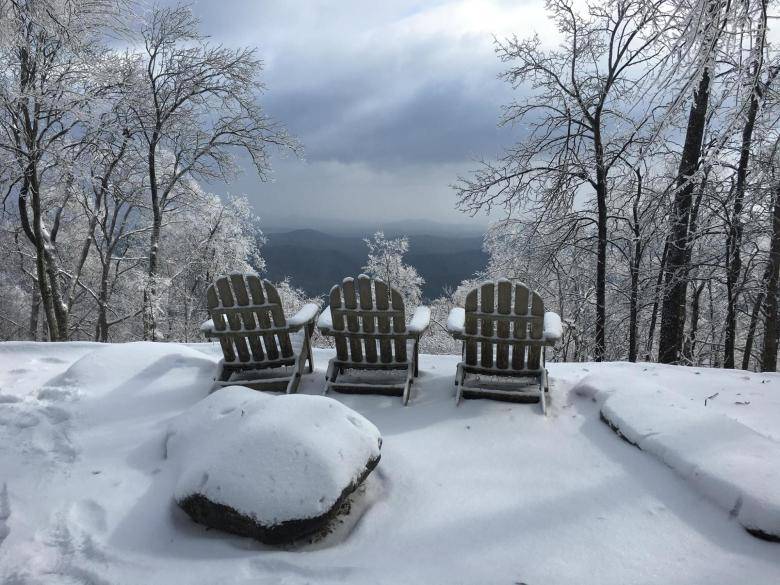 Three Adirondack chairs sit in a snowy clearing, overlooking a winter landscape in Atlanta, Georgia.