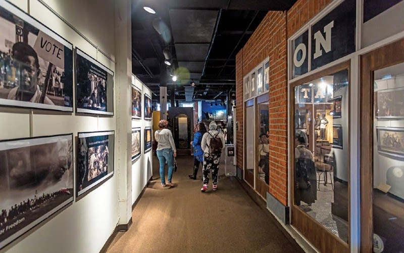 One Day Neighborhood Hopping Around Atlanta 5 Visitors walk through a dimly lit hallway adorned with historical photographs and posters, including one that reads 'VOTE' in Atlanta, Georgia.