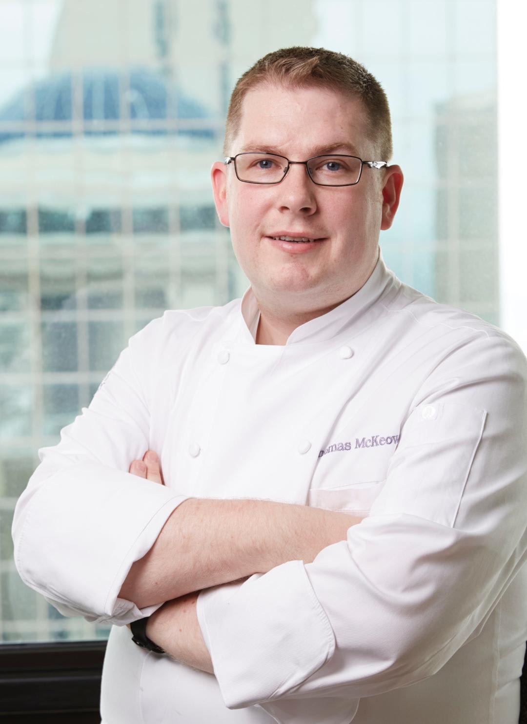 A smiling chef in a white uniform stands confidently with arms crossed in Atlanta, Georgia.
