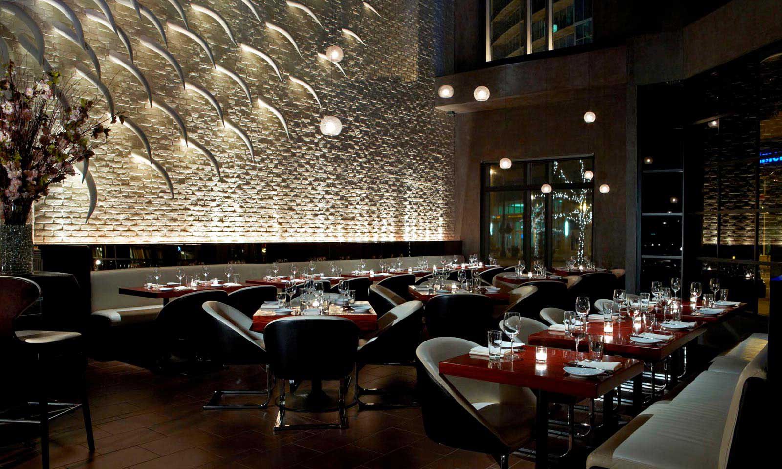 Modern restaurant interior with sleek black chairs, wooden tables, and a textured stone wall in Atlanta, Georgia.