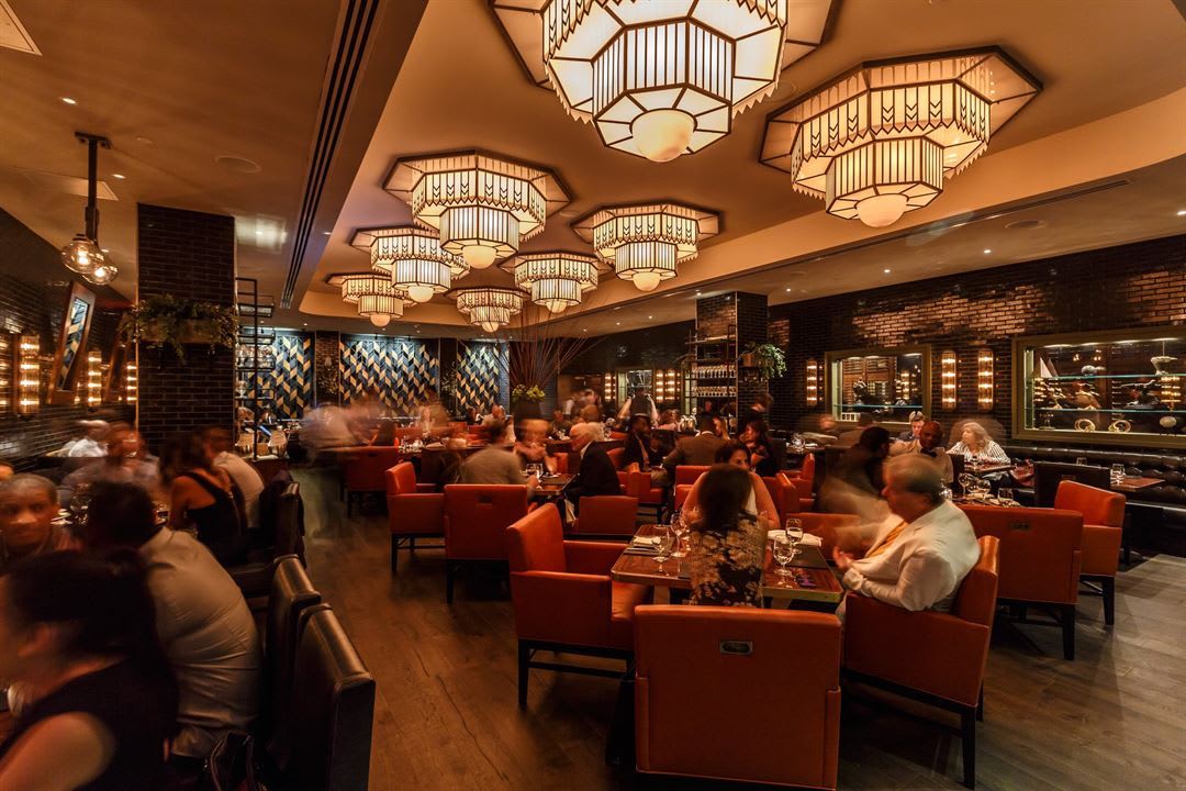 A bustling restaurant with orange chairs, black brick walls, and intricate chandeliers in Atlanta, Georgia.