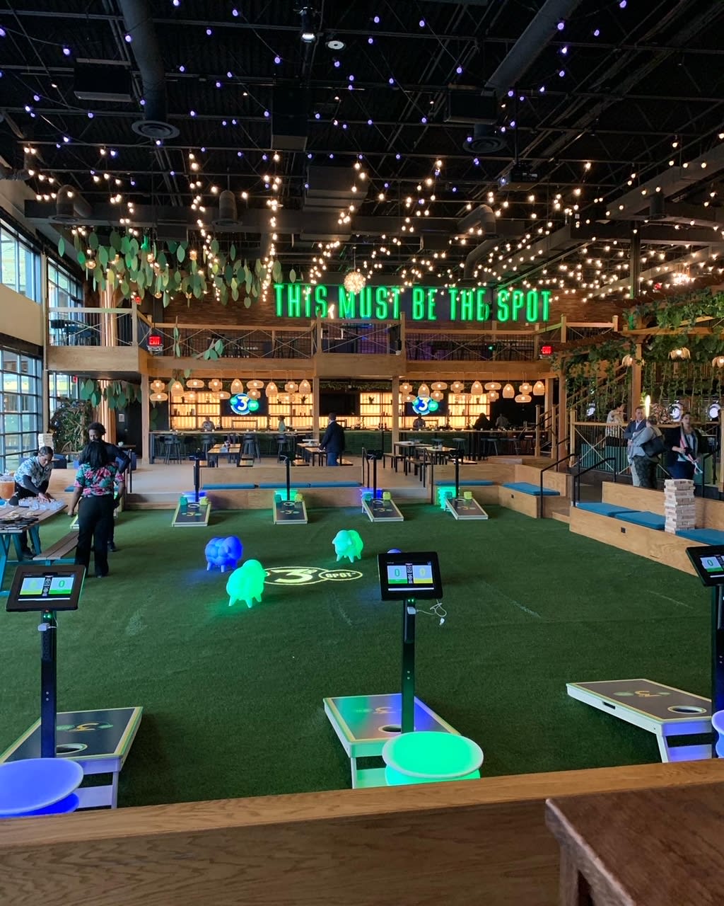 A modern indoor entertainment venue with a green turf floor, cornhole boards, and a bar area in Atlanta, Georgia.