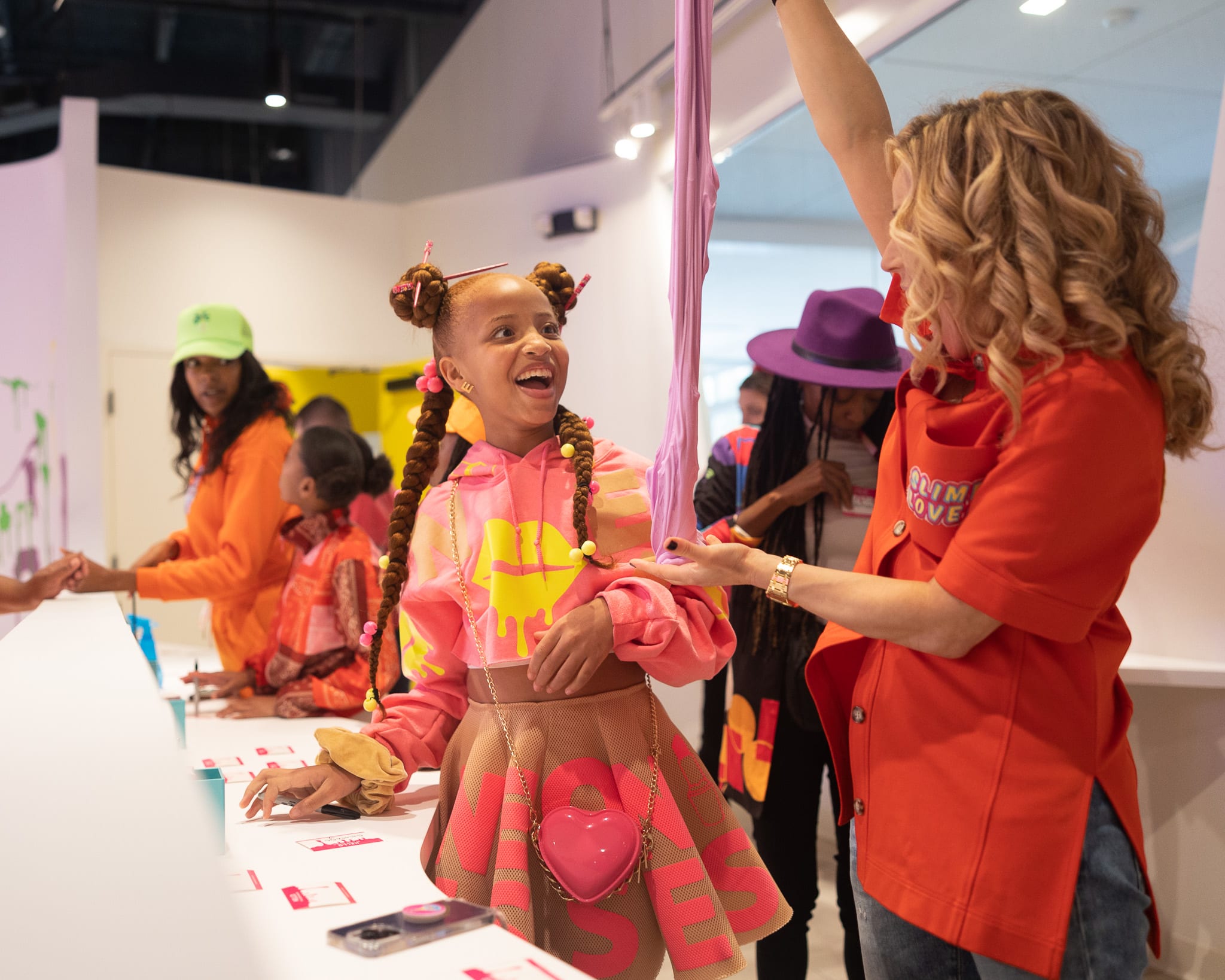 A young girl in a pink outfit with heart accessories is excitedly interacting with an adult at a colorful event in Atlanta, Georgia.