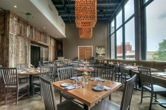 A spacious, rustic-modern restaurant with wooden tables, chairs, and a large, hanging light fixture in Atlanta, Georgia.