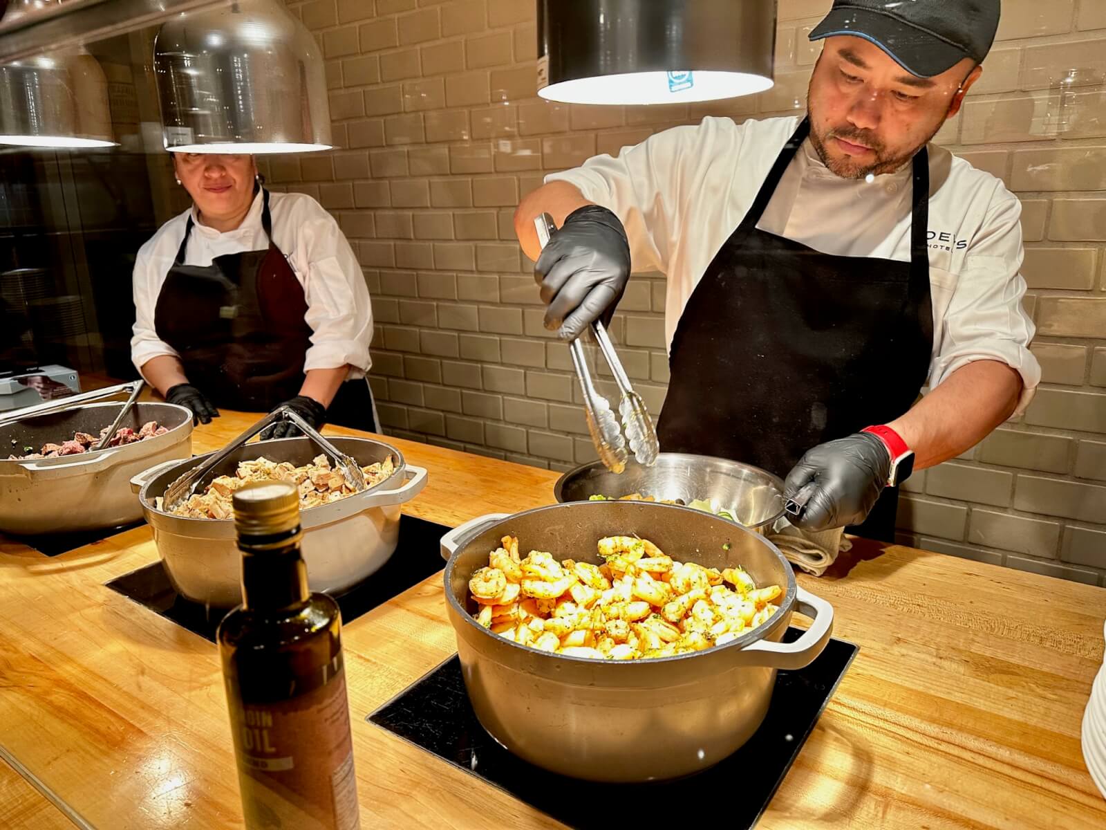 Two chefs in aprons and gloves prepare food in large pots on a kitchen counter in Atlanta, Georgia.
