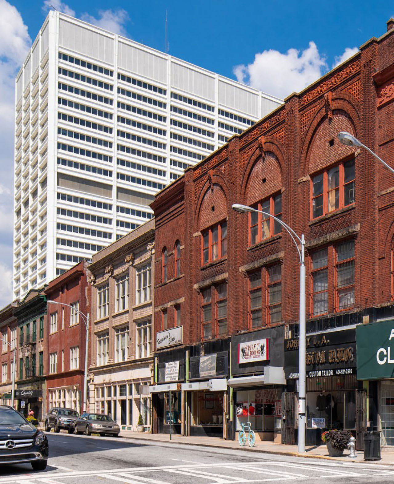 A city street lined with a mix of modern and historic buildings, featuring a tall white skyscraper and older red brick structures in Atlanta, Georgia.