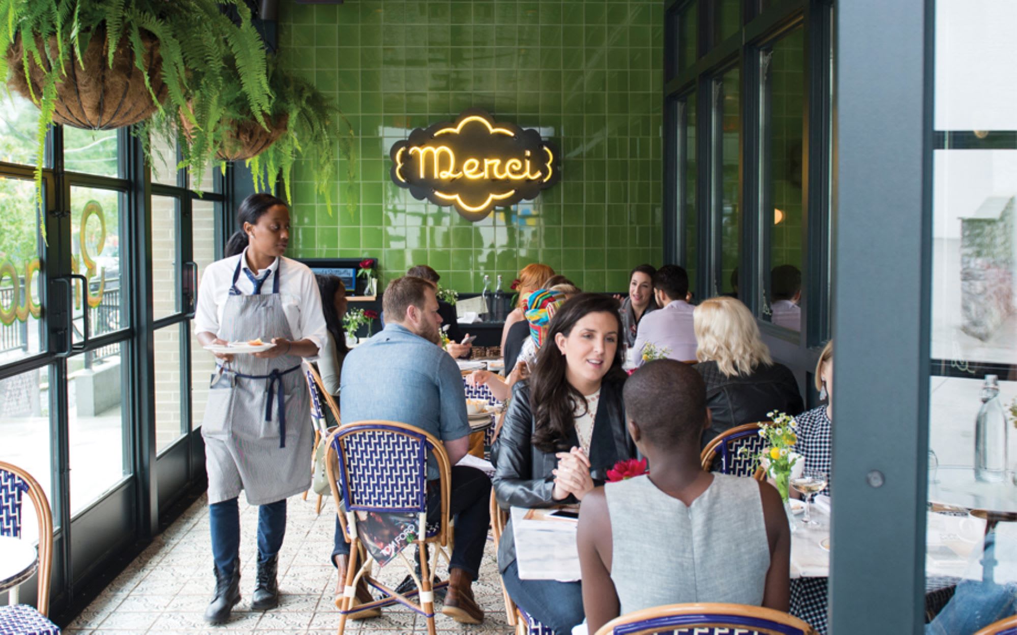 Patrons enjoy meals at a bustling restaurant with green walls and hanging plants in Atlanta, Georgia.
