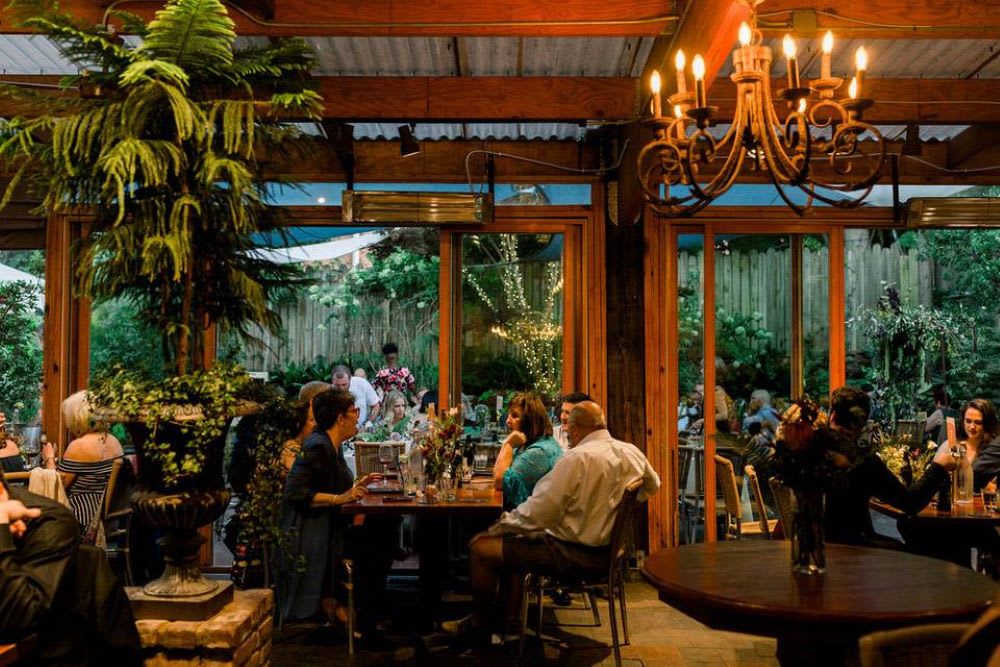 A lively restaurant with large windows, lush greenery, and diners enjoying meals at candlelit tables in Atlanta, Georgia.