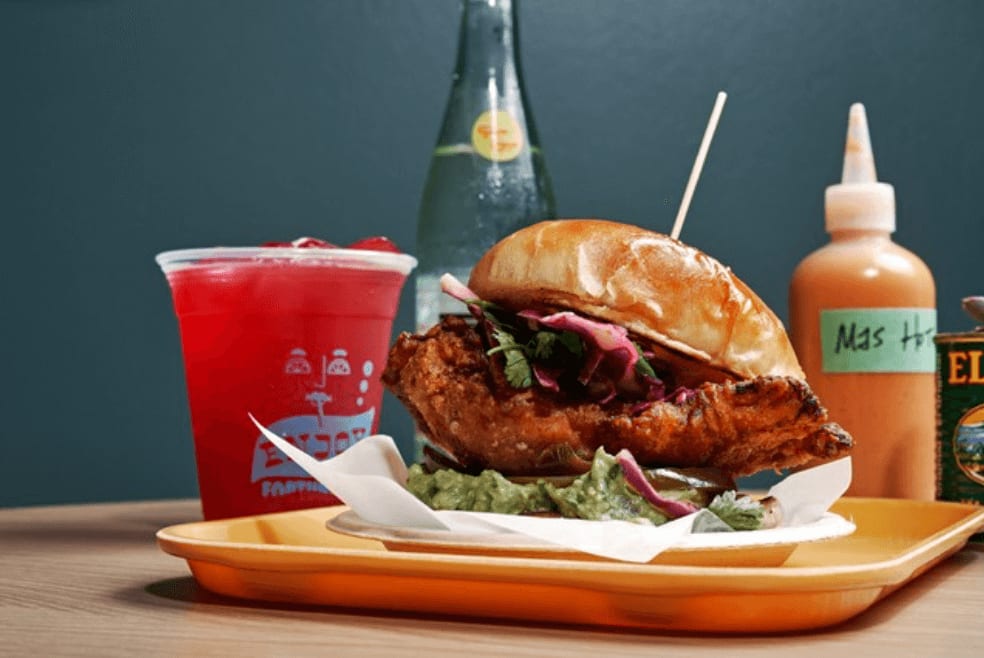 A vibrant meal featuring a fried chicken sandwich with guacamole and red drink in Atlanta, Georgia.