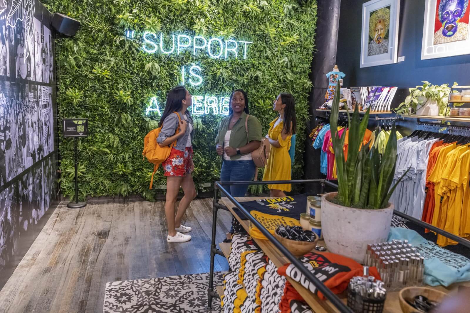 Three women stand in a colorful clothing store with a green wall and neon sign in Atlanta, Georgia.