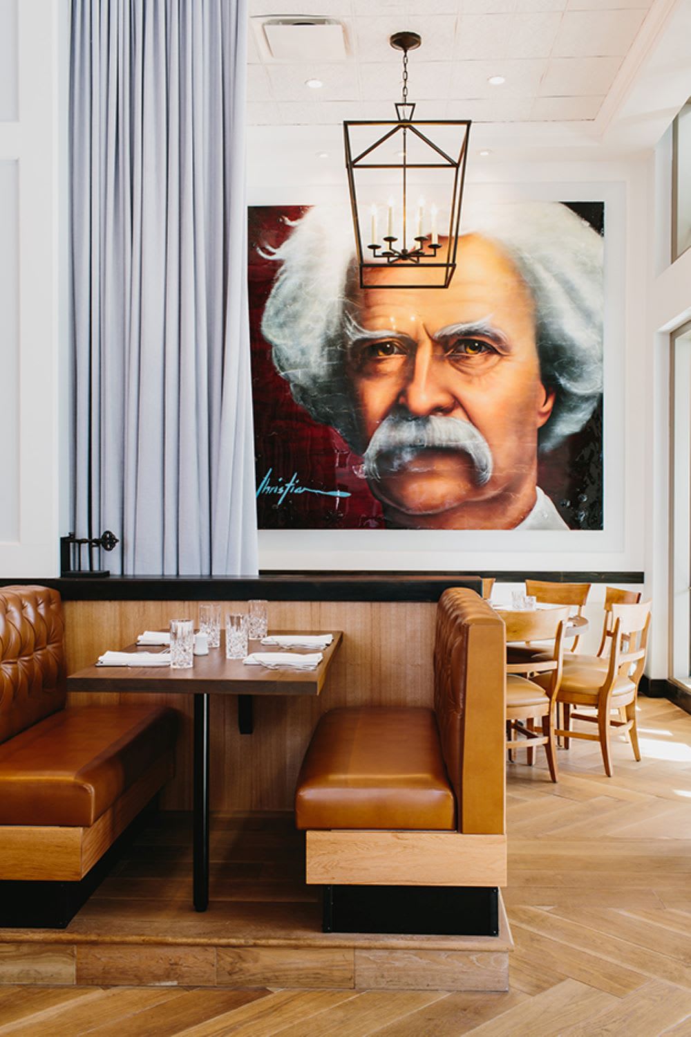 A restaurant booth with leather seats and a wooden table, illuminated by a chandelier, sits in front of a large portrait of Albert Einstein in Atlanta, Georgia.