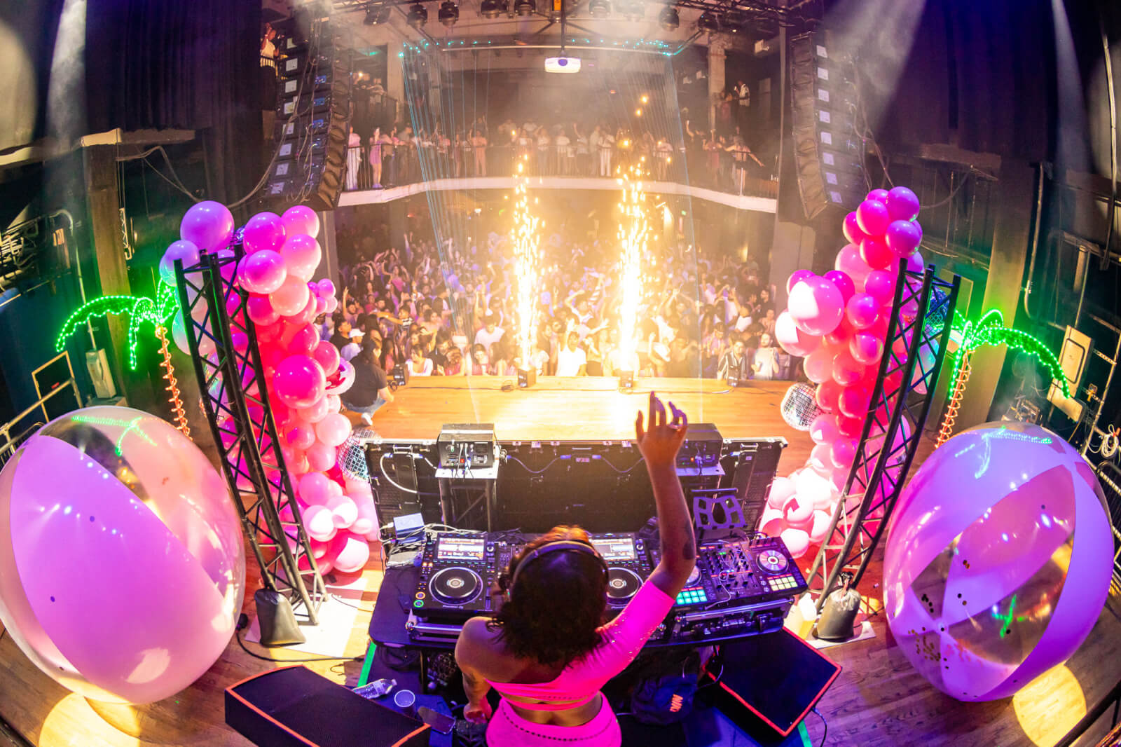 A DJ performs at a vibrant concert with a crowd of people, pink balloons, and fireworks in Atlanta, Georgia.