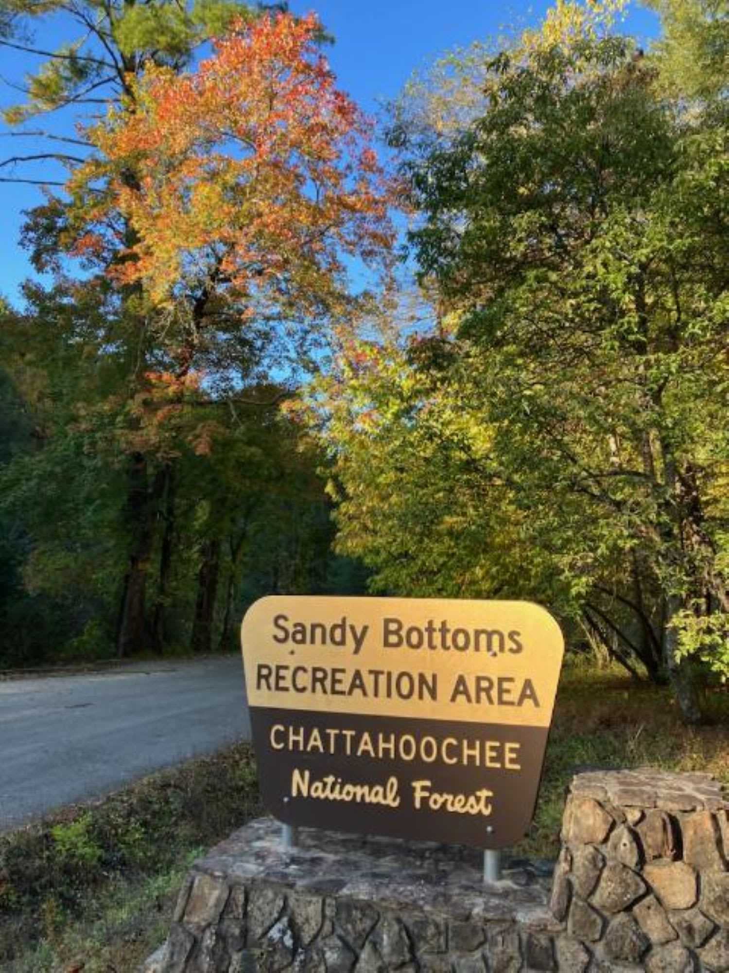 A wooden sign marks the entrance to a forest recreation area with colorful autumn trees in Atlanta, Georgia.
