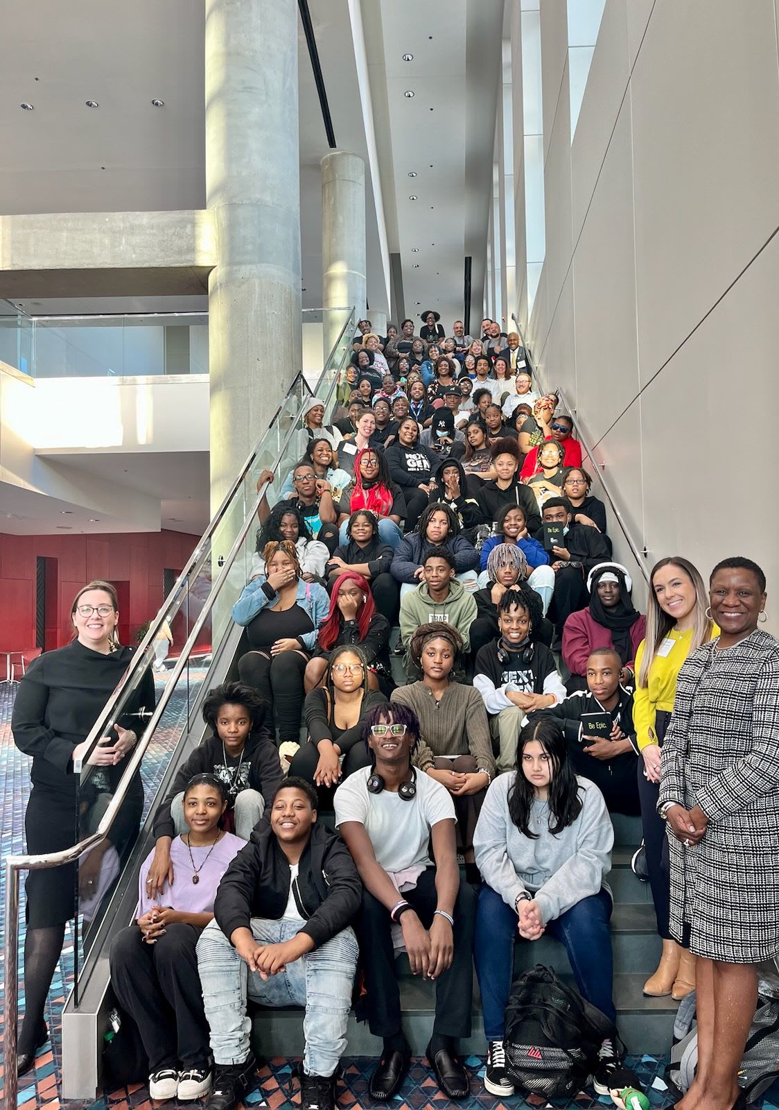 A diverse group of young people, mostly Black, pose on a staircase in a modern building in Atlanta, Georgia.