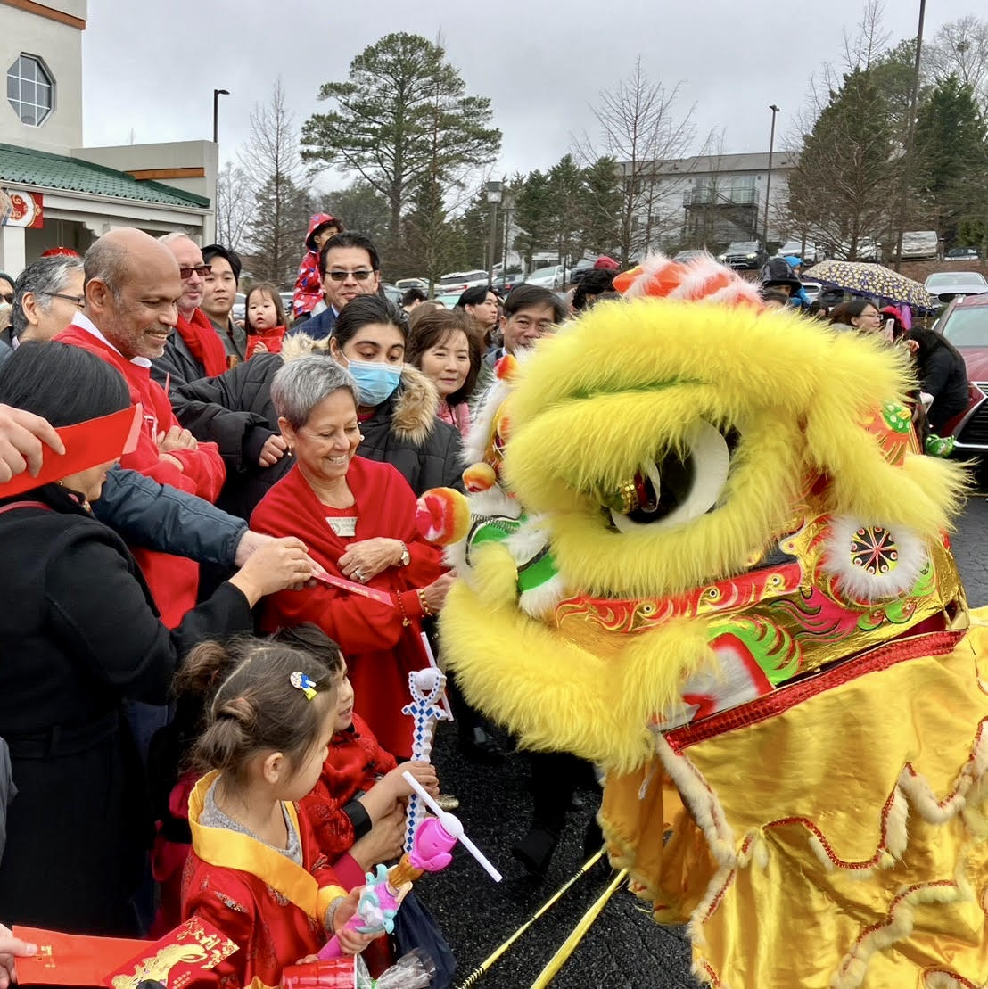 Crowd gathers around a vibrant yellow lion dance performer at a festive outdoor event in Atlanta, Georgia.