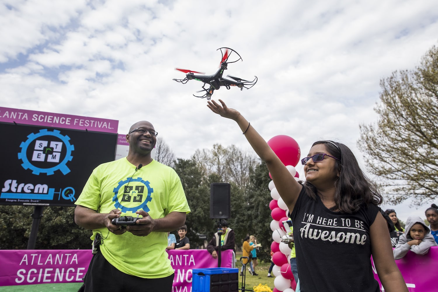 Two people at a science festival control a drone flying overhead in Atlanta, Georgia.