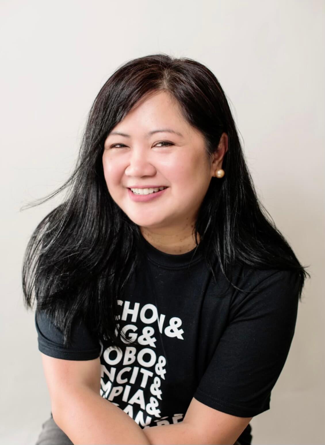 A smiling woman with long black hair wearing a black t-shirt with white text in Atlanta, Georgia.