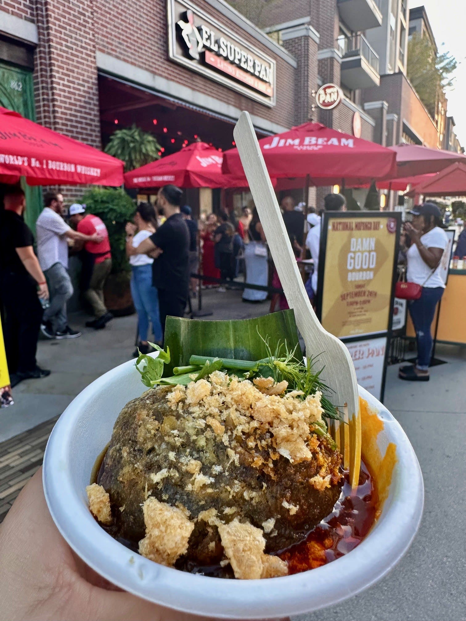 A hand holds a bowl of crispy fried food with herbs and sauce, outdoors at a food event in Atlanta, Georgia.
