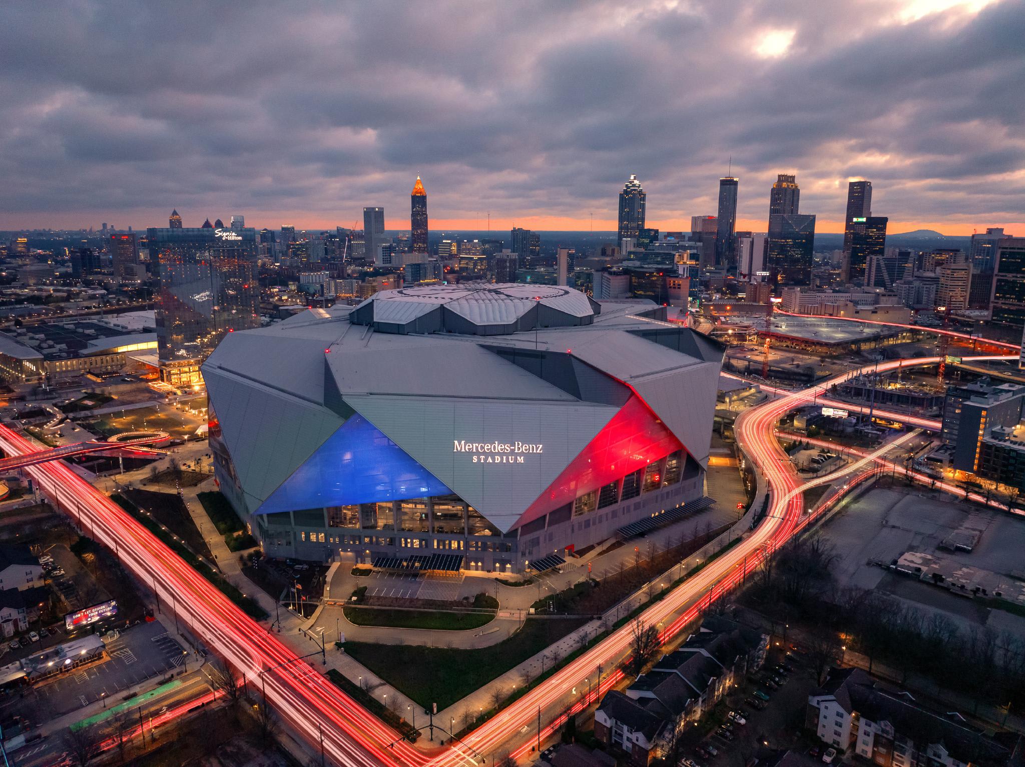 Aerial view of Mercedes-Benz Stadium at dusk, surrounded by city lights and highways in Atlanta, Georgia.