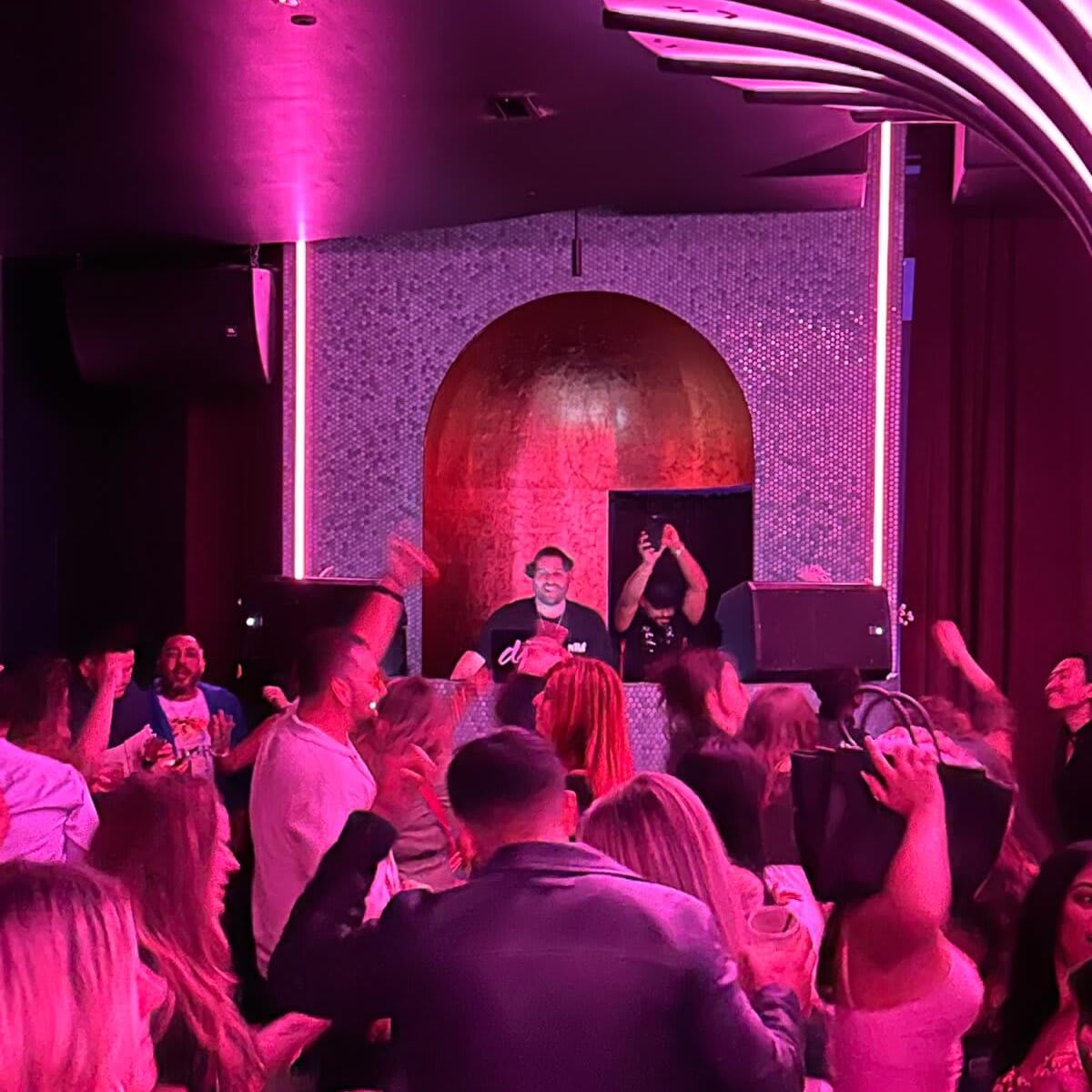 Crowded nightclub scene with DJ on stage, pink lighting, and energetic dancers in Atlanta, Georgia.
