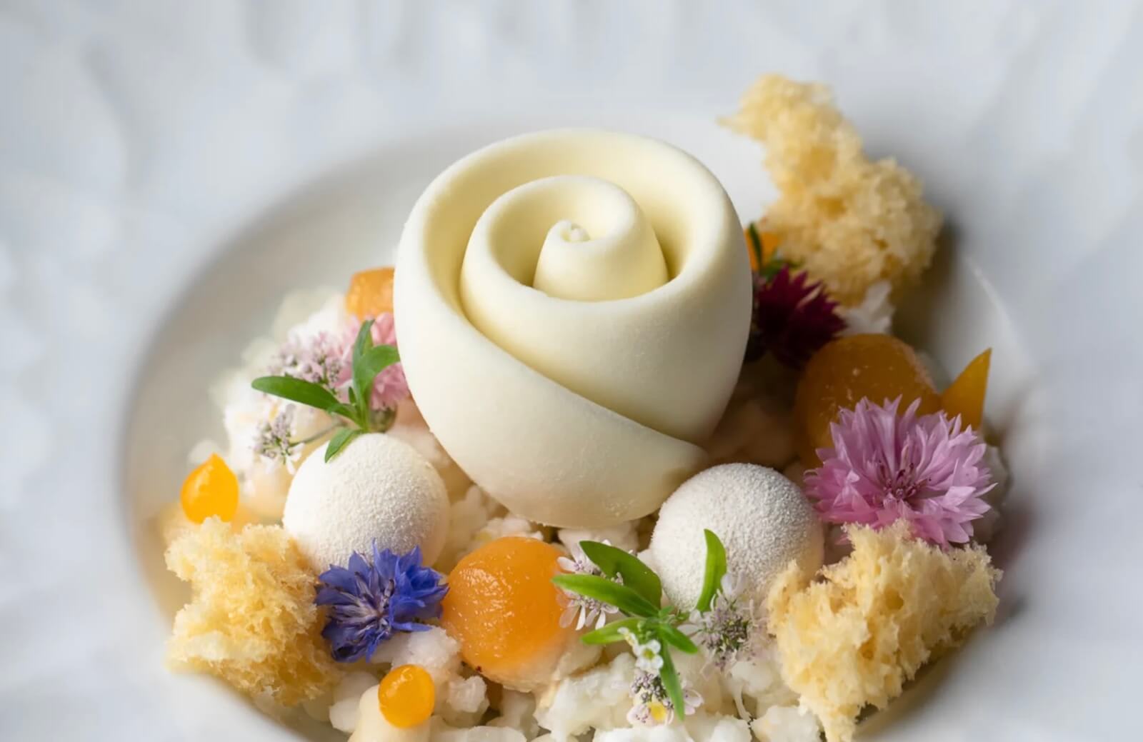 A delicate white rose-shaped dessert with colorful edible flowers and citrus accents in Atlanta, Georgia.