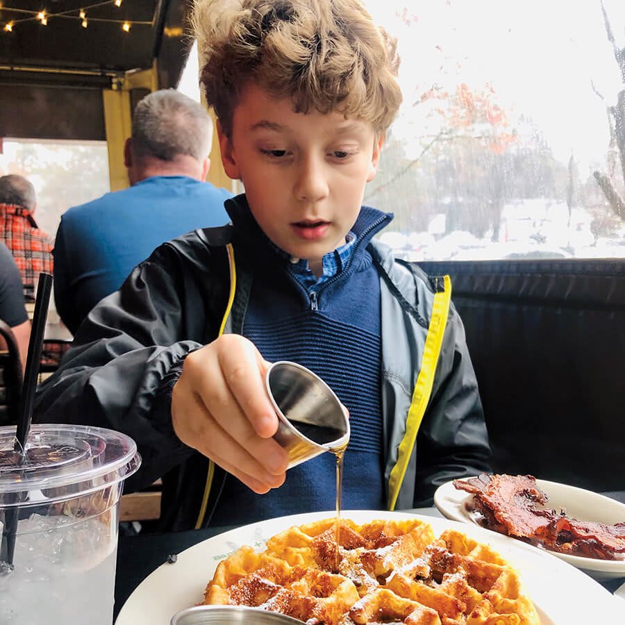 A young boy pours syrup over waffles at a restaurant table in Atlanta, Georgia.