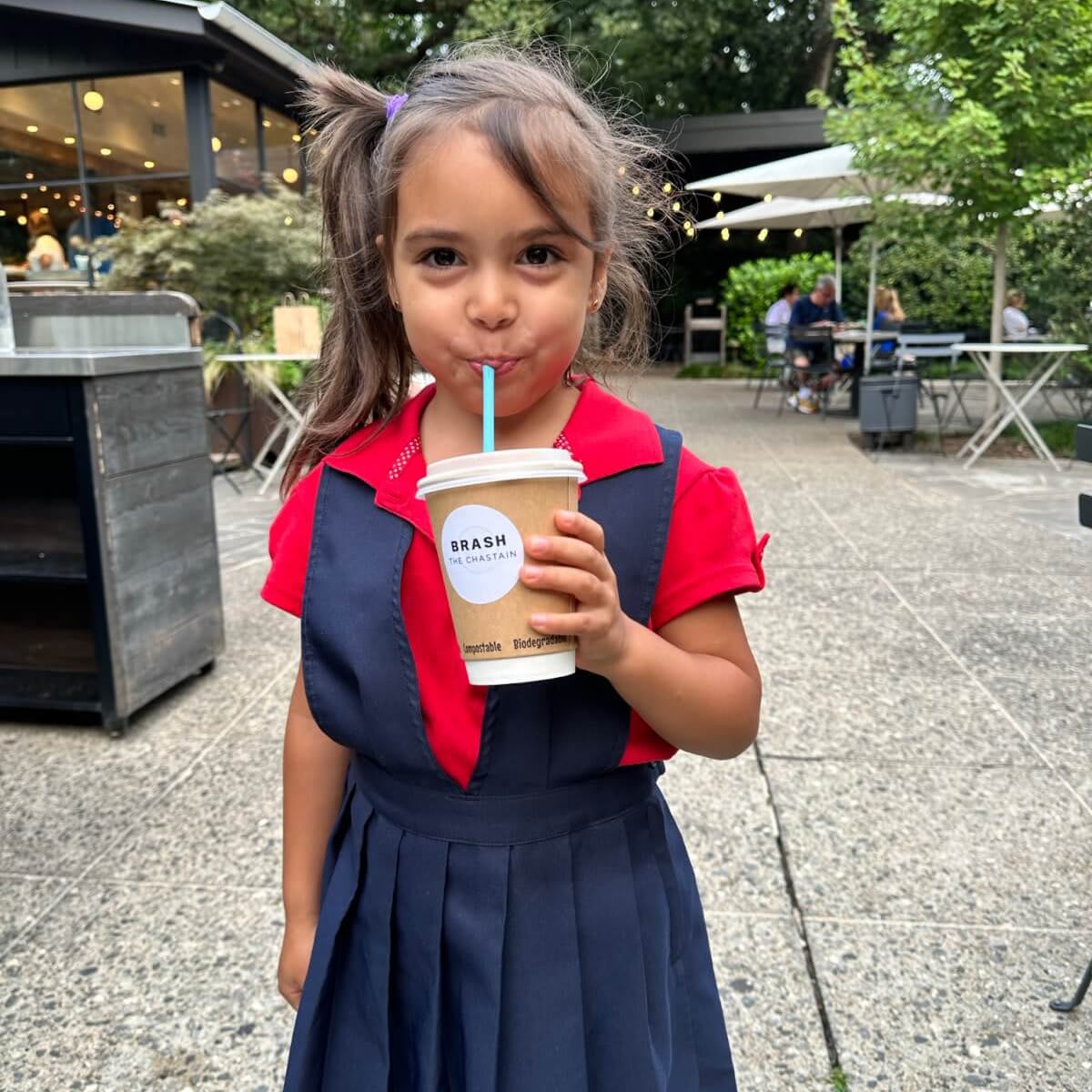 A young girl in a red and blue school uniform enjoys a drink with a straw outdoors in Atlanta, Georgia.