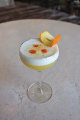 A glass of yellow cocktail with orange peel and red dots on top in Atlanta, Georgia.