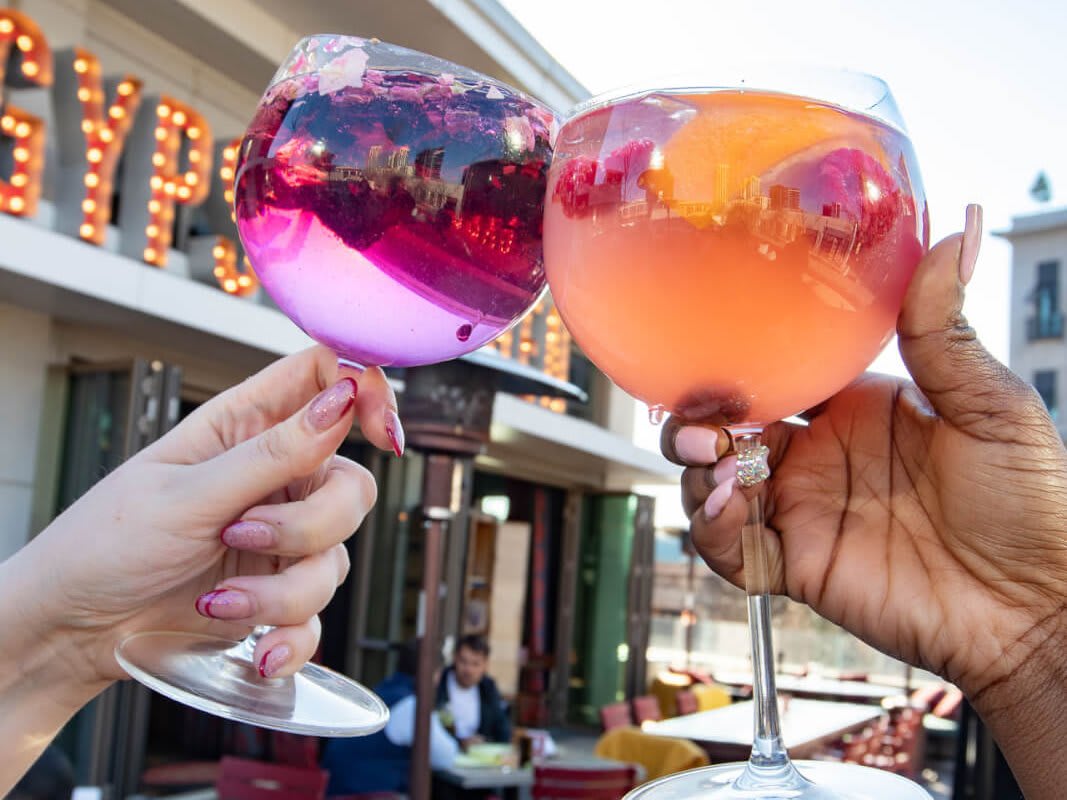 Two hands clink colorful cocktails in a celebratory toast outside a restaurant in Atlanta, Georgia.