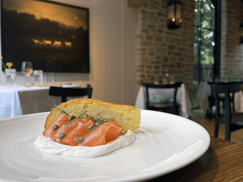 A white plate with smoked salmon, capers, dill, and sour cream on a wooden table in a restaurant in Atlanta, Georgia.