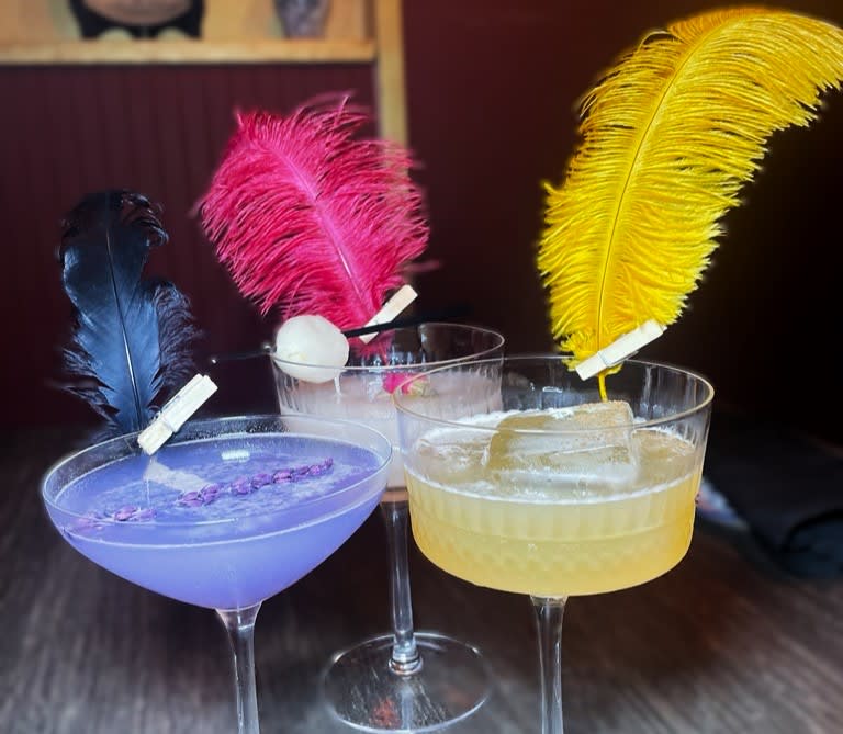 Three colorful cocktails with feather garnishes in elegant glasses on a wooden table in Atlanta, Georgia.
