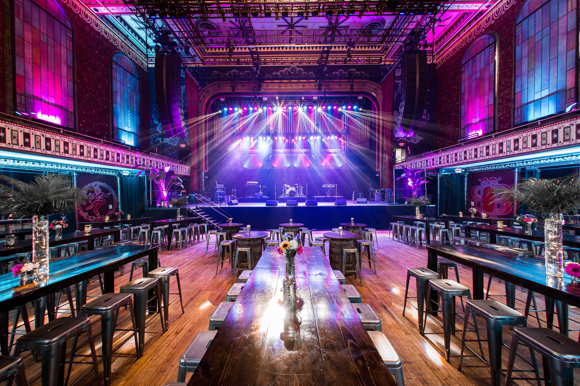 A vibrant, ornate concert hall with a stage bathed in colorful lights and rows of tables and stools in Atlanta, Georgia.