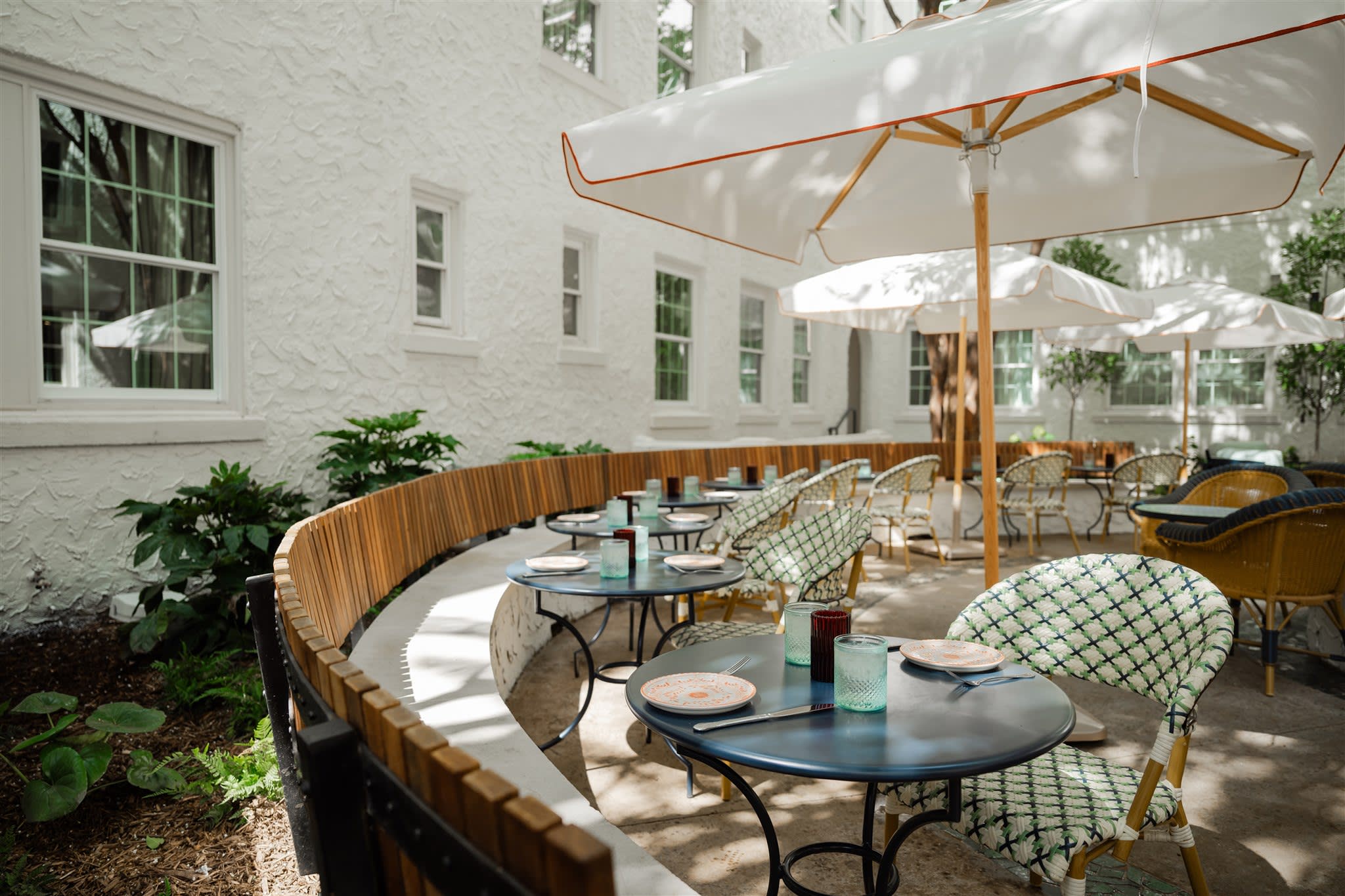 Outdoor seating area with round tables, patterned chairs, and umbrellas in a garden setting in Atlanta, Georgia.