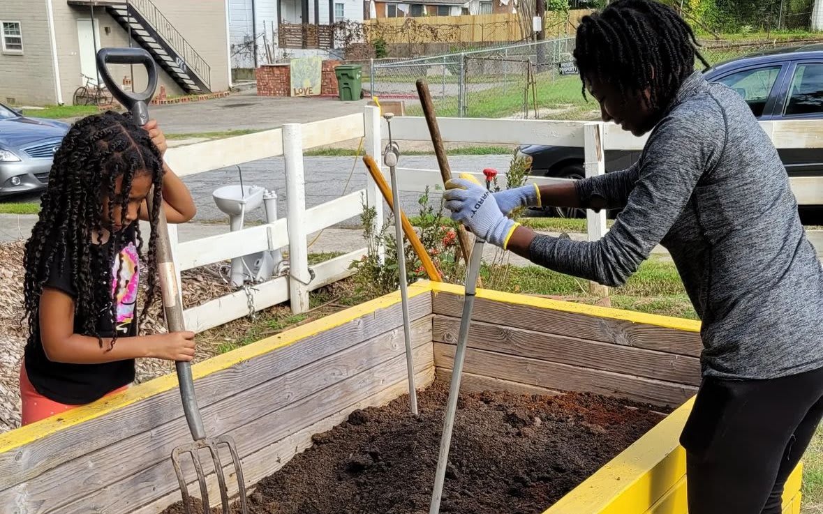 Two people, one adult and one child, are gardening together in a raised bed in Atlanta, Georgia.
