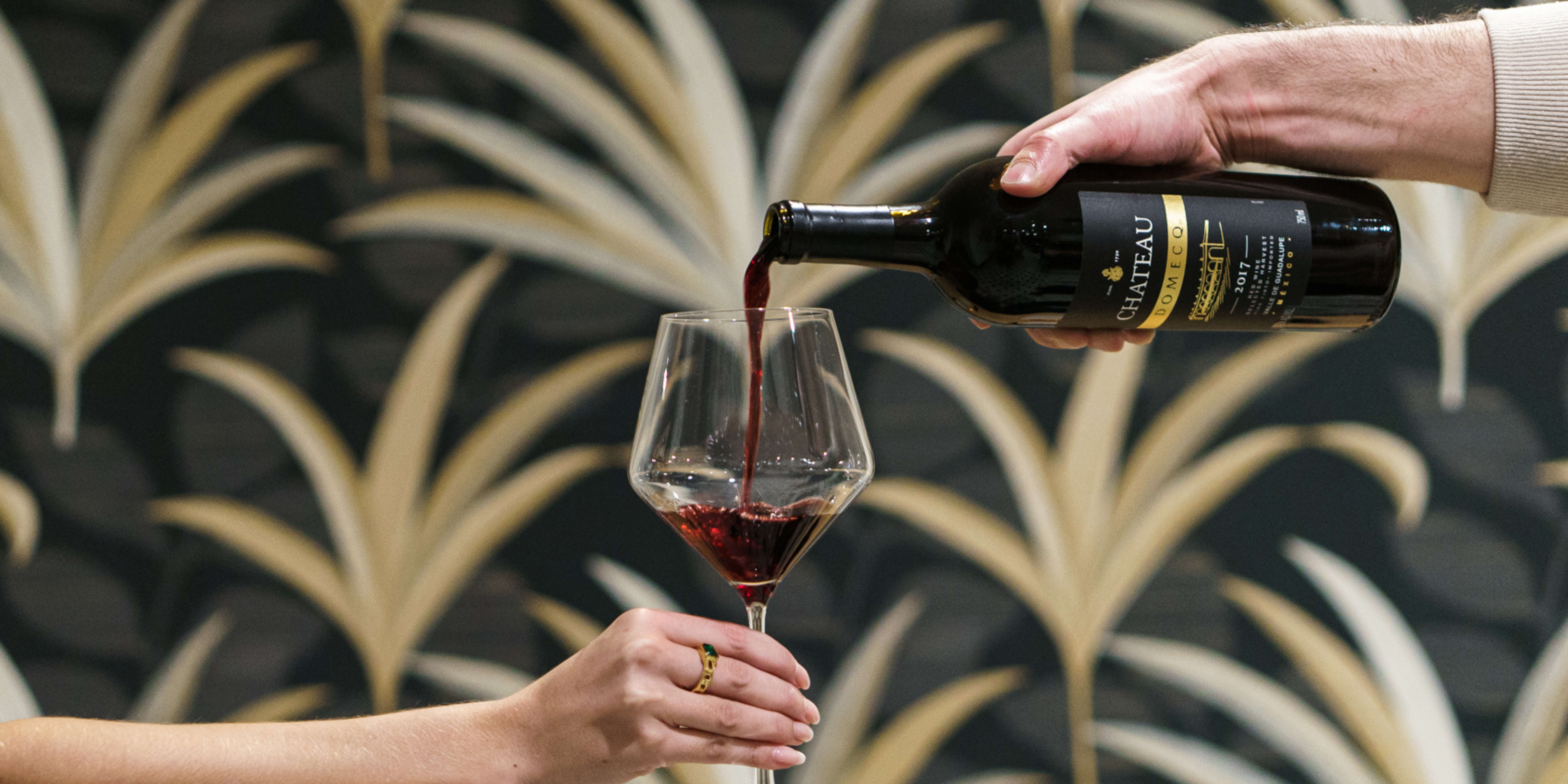 A hand pours red wine from a bottle labeled 'Chateau' into a glass held by another hand in Atlanta, Georgia.
