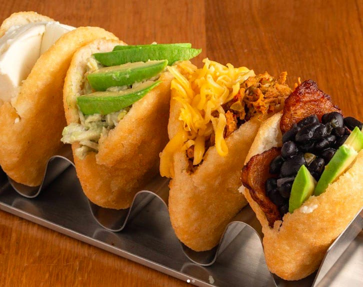 Four different types of arepas displayed in a metal holder on a wooden table in Atlanta, Georgia.