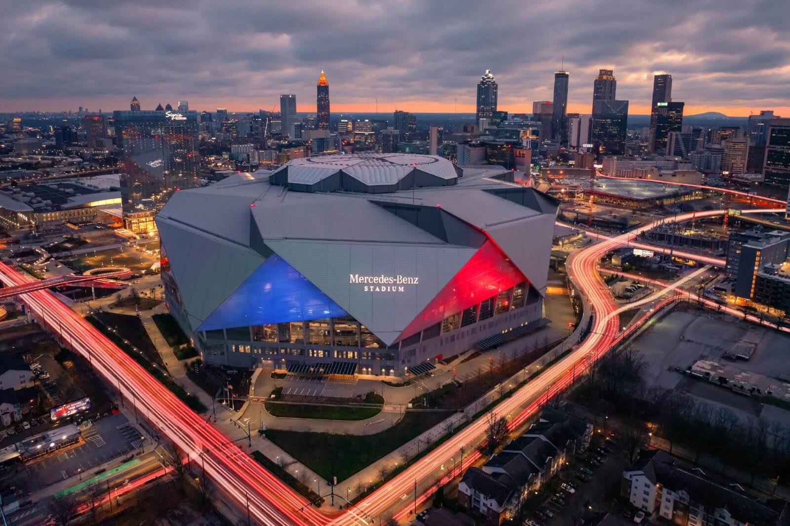 Aerial view of illuminated Mercedes-Benz Stadium at night with city skyline in background in Atlanta, Georgia.