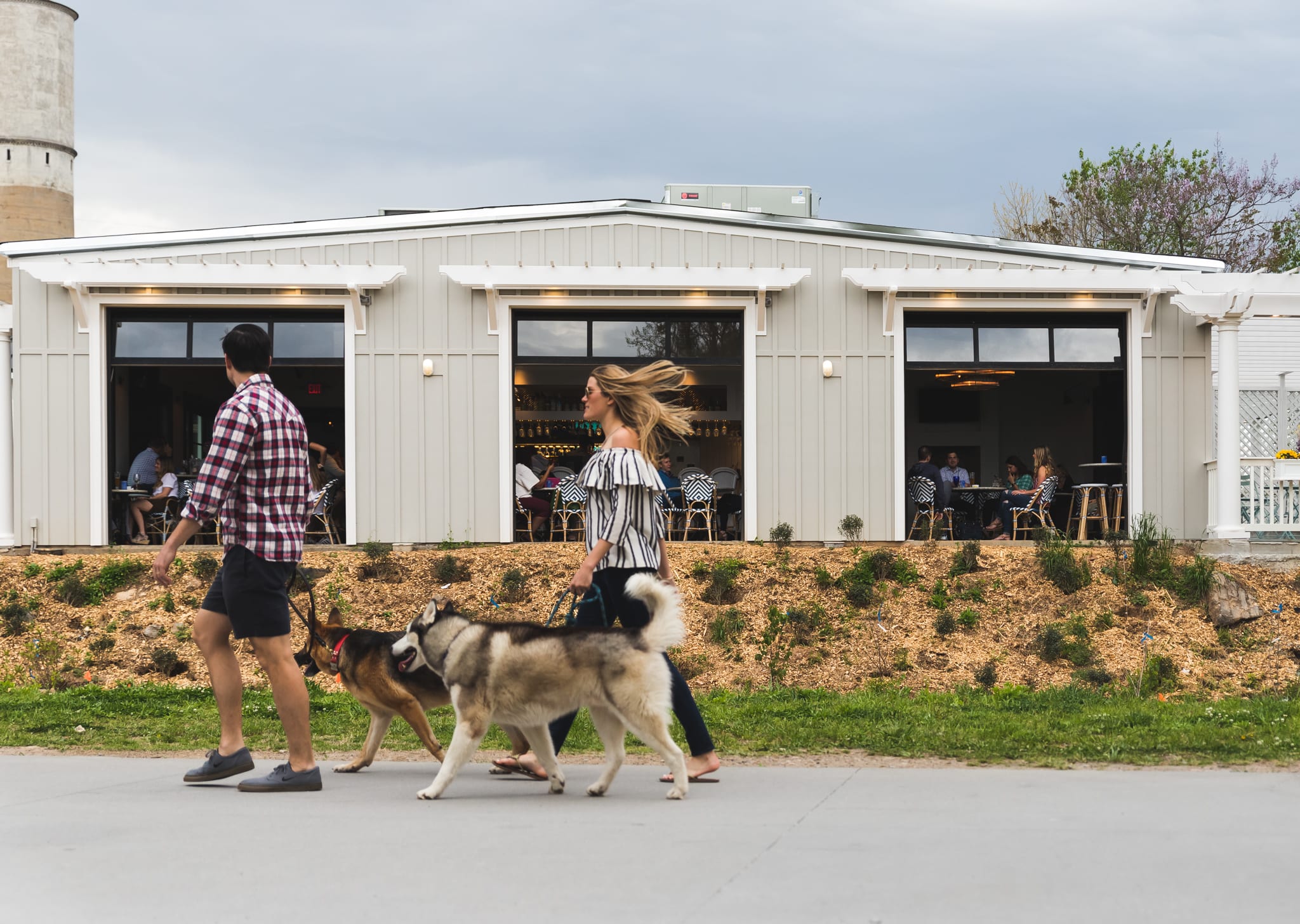A couple walks three dogs past a restaurant with outdoor seating at dusk in Atlanta, Georgia.