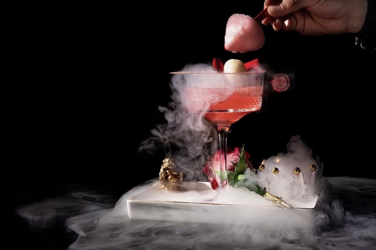 A hand adds a pink cotton candy topping to a smoky, rose-adorned cocktail in a glass in Atlanta, Georgia.