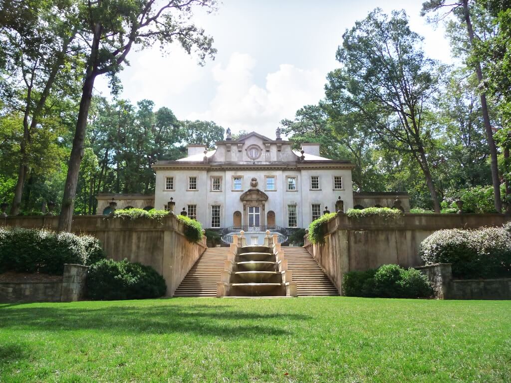 A grand white mansion with a central staircase and fountain, surrounded by lush greenery in Atlanta, Georgia.