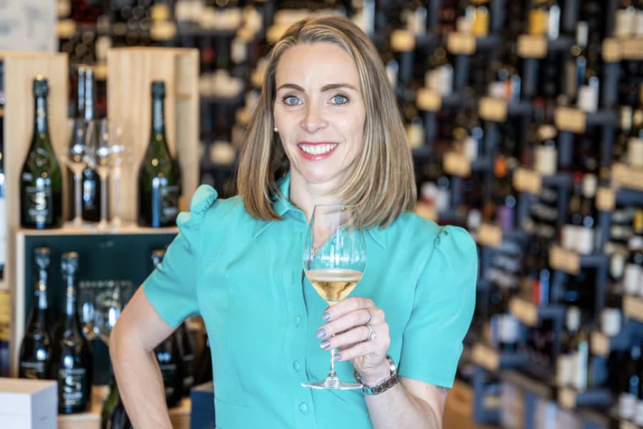 A woman in a teal blouse smiles while holding a glass of white wine in a wine shop in Atlanta, Georgia.