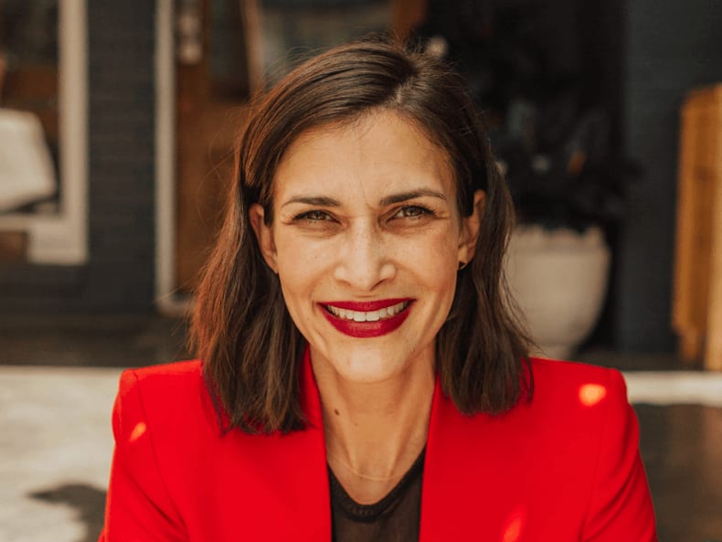 A woman with shoulder-length dark hair smiles brightly, wearing a vibrant red blazer in Atlanta, Georgia.
