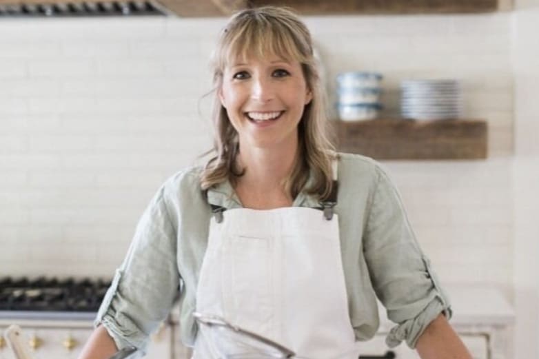 A woman in a kitchen smiles while wearing an apron and standing near a stove in Atlanta, Georgia.