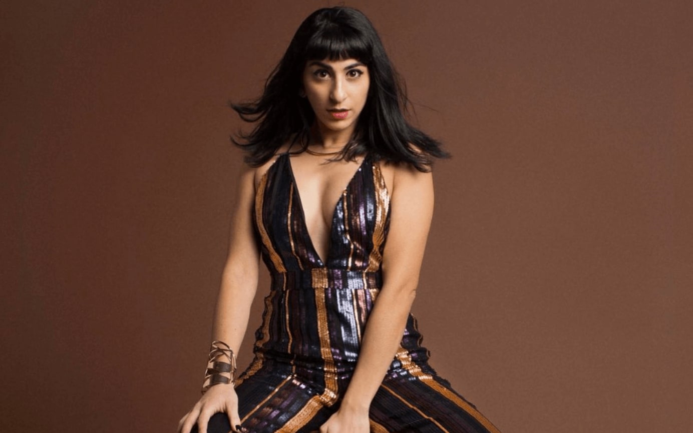 A woman with long dark hair sits wearing a shimmering, striped, low-cut jumpsuit in Atlanta, Georgia.
