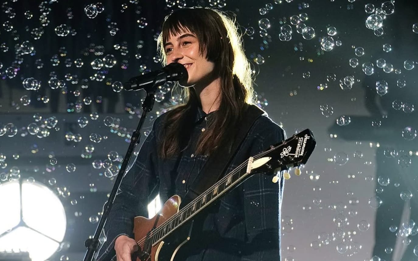 A musician with long hair plays an electric guitar and sings into a microphone on stage in Atlanta, Georgia.