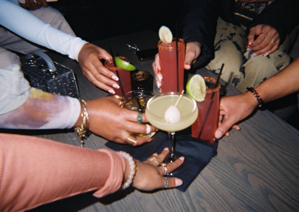 A group of friends raise colorful cocktails in a celebratory toast around a table in Atlanta, Georgia.