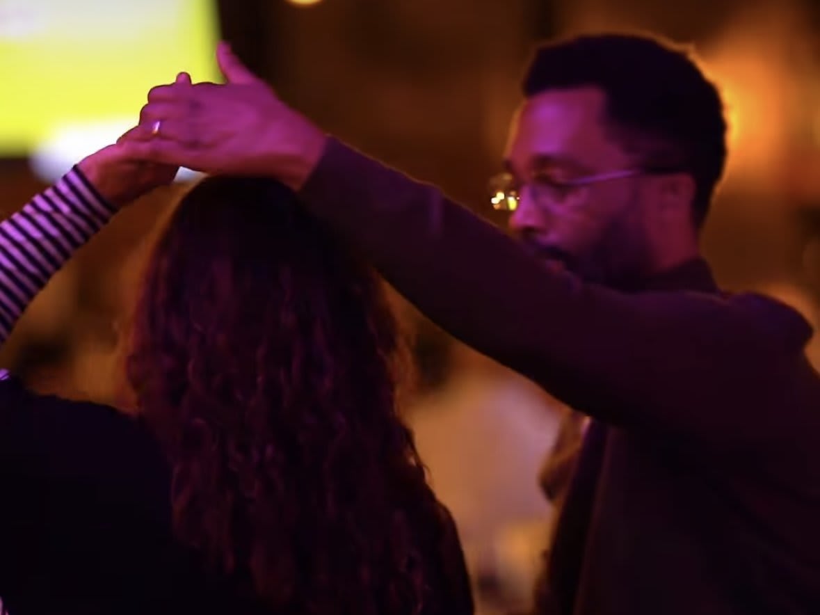 A man and woman dance together, holding hands, in a dimly lit room with a yellow screen in the background in Atlanta, Georgia.